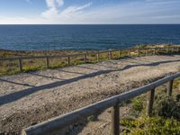 a wooden walkway over looking the ocean on a clear day in the sun near a path