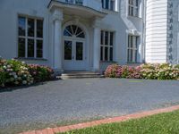 a large white building with flowers growing in front of it and grass and flowers by the entrance