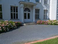 a large white building with flowers growing in front of it and grass and flowers by the entrance