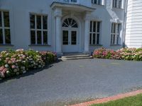 a large white building with flowers growing in front of it and grass and flowers by the entrance