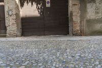 the building with an open doorway is on cobblestone pavement near a wooden door