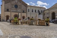 an outdoor restaurant is being set up next to a street side church with cars and tables