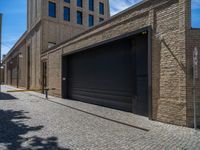 two windows in the side of a brick building, with a black garage door and brown door