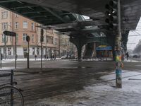 a couple bikes are parked underneath a train station covered with snow by a snowy street