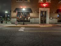 a street is dark and has buildings, a lamp pole, and the sidewalk with some lights on it