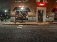 a street is dark and has buildings, a lamp pole, and the sidewalk with some lights on it