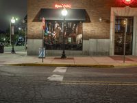 a street is dark and has buildings, a lamp pole, and the sidewalk with some lights on it