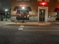 a street is dark and has buildings, a lamp pole, and the sidewalk with some lights on it