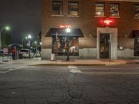 a street is dark and has buildings, a lamp pole, and the sidewalk with some lights on it