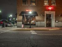 a street is dark and has buildings, a lamp pole, and the sidewalk with some lights on it