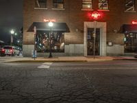 a street is dark and has buildings, a lamp pole, and the sidewalk with some lights on it