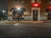 a street is dark and has buildings, a lamp pole, and the sidewalk with some lights on it