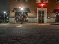 a street is dark and has buildings, a lamp pole, and the sidewalk with some lights on it