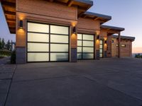 a garage area in the evening with lights on the side and two large garage doors on the inside