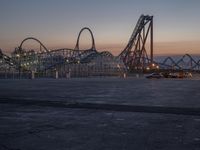 the sun is setting over a roller coaster and car parking lot with an empty car