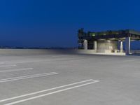 a small parking structure sits in the evening hours on a concrete lot with lots of space for walking or running