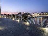 an outdoor walkway with lights, railings, and a river at dusk time in the background