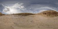 360 view of dirt terrain, clouds and mountains in distance, with sun peaking through the clouds