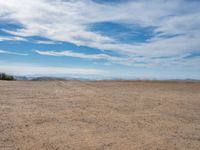 an empty dirt field with bare trees on top and some blue sky in the distance