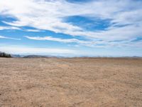 an empty dirt field with bare trees on top and some blue sky in the distance