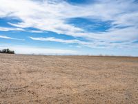 an empty dirt field with bare trees on top and some blue sky in the distance