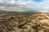 an expansive view of a desert on a cloudy day with mountains in the background as the sun shines on the mountains