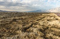 an expansive view of a desert on a cloudy day with mountains in the background as the sun shines on the mountains