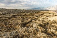 an expansive view of a desert on a cloudy day with mountains in the background as the sun shines on the mountains