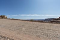 a dirt road in a dry area with a house on the other side and mountains in the background