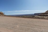 a dirt road in a dry area with a house on the other side and mountains in the background