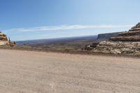 a dirt road in a dry area with a house on the other side and mountains in the background