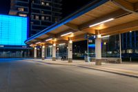 a bus station is at night by some buildings with lights on it's pillars