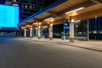 a bus station is at night by some buildings with lights on it's pillars