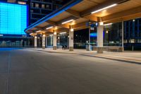 a bus station is at night by some buildings with lights on it's pillars