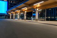 a bus station is at night by some buildings with lights on it's pillars