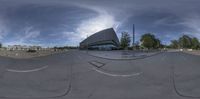 this is a fish - eye shot of a building by the road with a bench and a street car