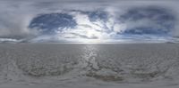 a very large cloudy sky is above the beach and water, there are footprints in the wet sand