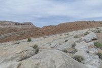 a person on top of some big rocks near a hill, and some hills behind the field and the mountain