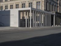 an exterior view of a building with pillars and a person walking on the sidewalk in front