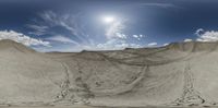 a view of a sand dune area with clouds in the sky and a sun shining brightly on a sunny day