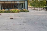 someone has fallen down to his skateboard in a courtyard of a building with bushes and trees