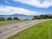 a dirt road near a body of water and a hill in the distance with trees on it