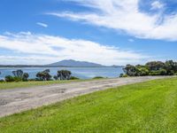 a dirt road near a body of water and a hill in the distance with trees on it