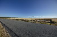 a country road passing by an open field with a fence in the middle of the photo