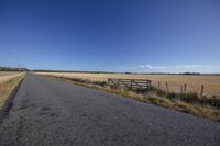 a country road passing by an open field with a fence in the middle of the photo