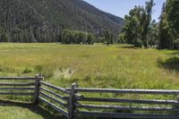 this is the fence that separates two pasture areas of land next to mountains and a meadow