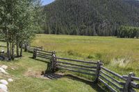 this is the fence that separates two pasture areas of land next to mountains and a meadow