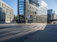 city street with an empty street with cars driving past it and a large glass building in the background