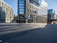 city street with an empty street with cars driving past it and a large glass building in the background