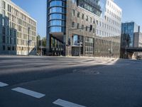 city street with an empty street with cars driving past it and a large glass building in the background